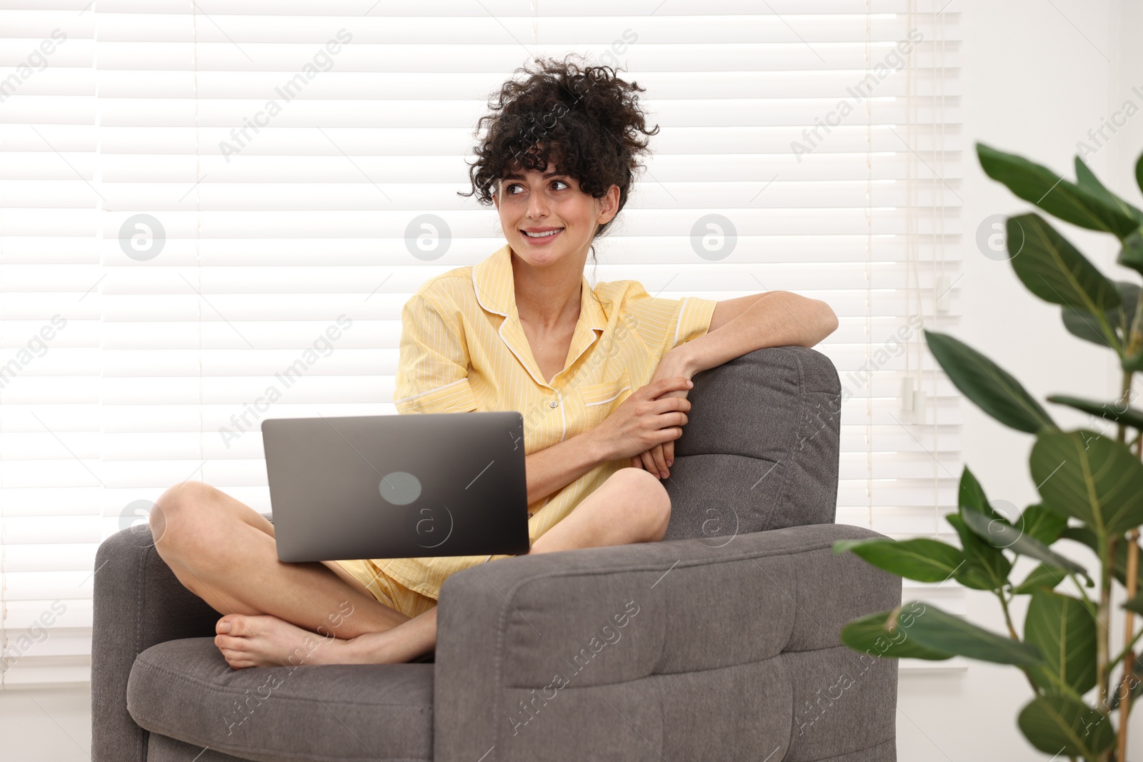 Photo of Beautiful young woman in stylish pyjama with laptop on armchair at home