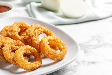 Photo of Plate with homemade crunchy fried onion rings on marble table, closeup. Space for text
