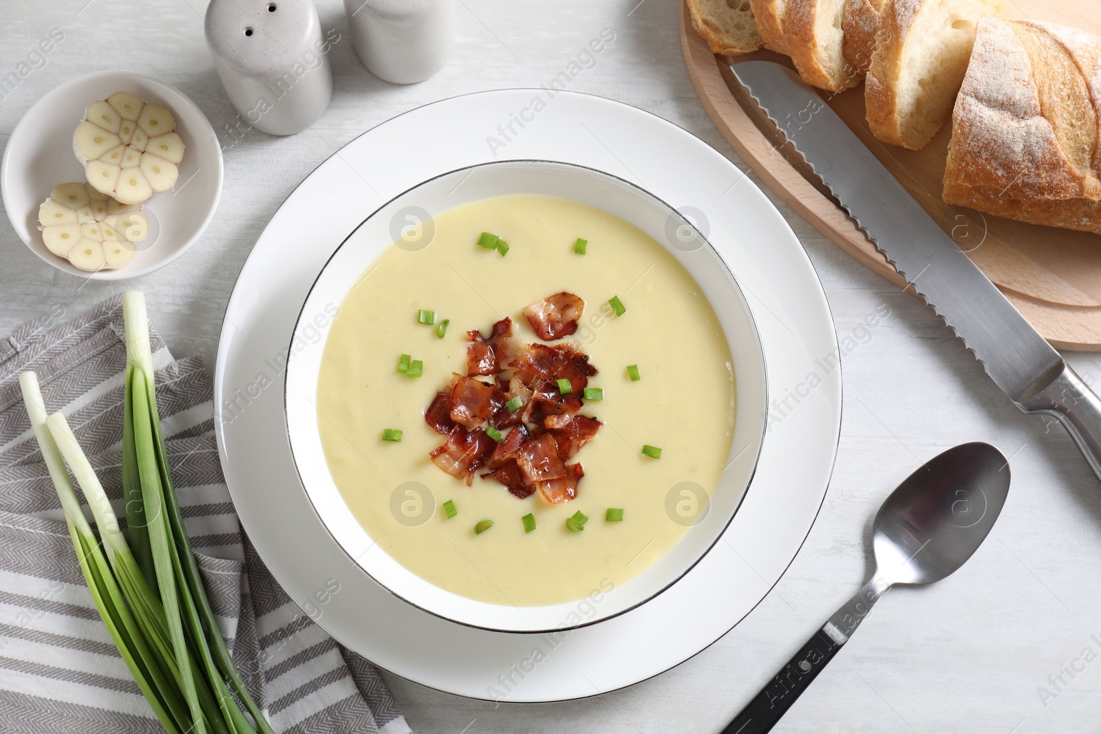 Photo of Tasty potato soup with bacon in bowl served on white wooden table, flat lay