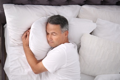 Photo of Man sleeping on comfortable pillow in bed at home, top view