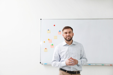 Portrait of young teacher near whiteboard in classroom. Space for text