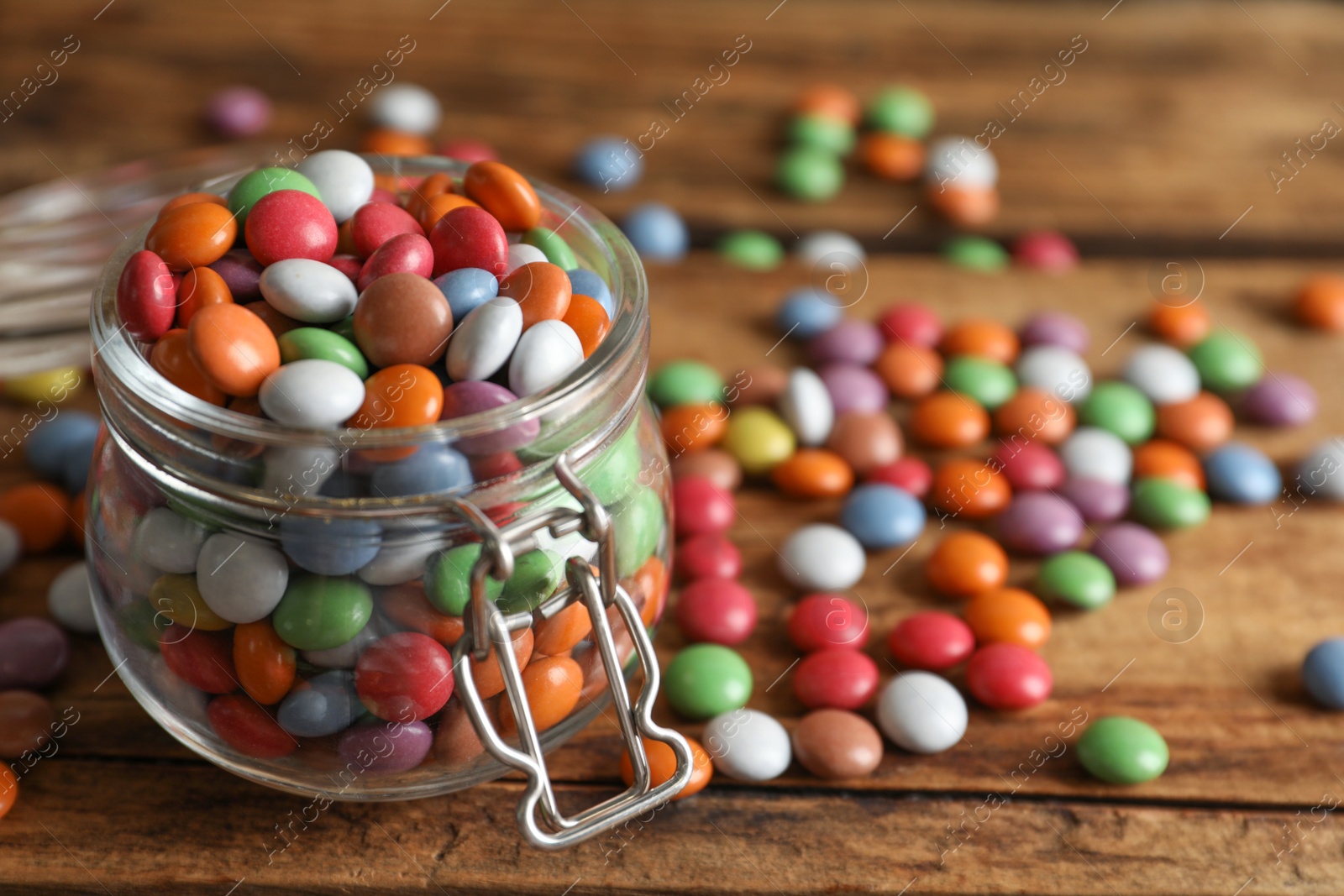 Photo of Delicious dragee in jar on wooden table, closeup. Space for text