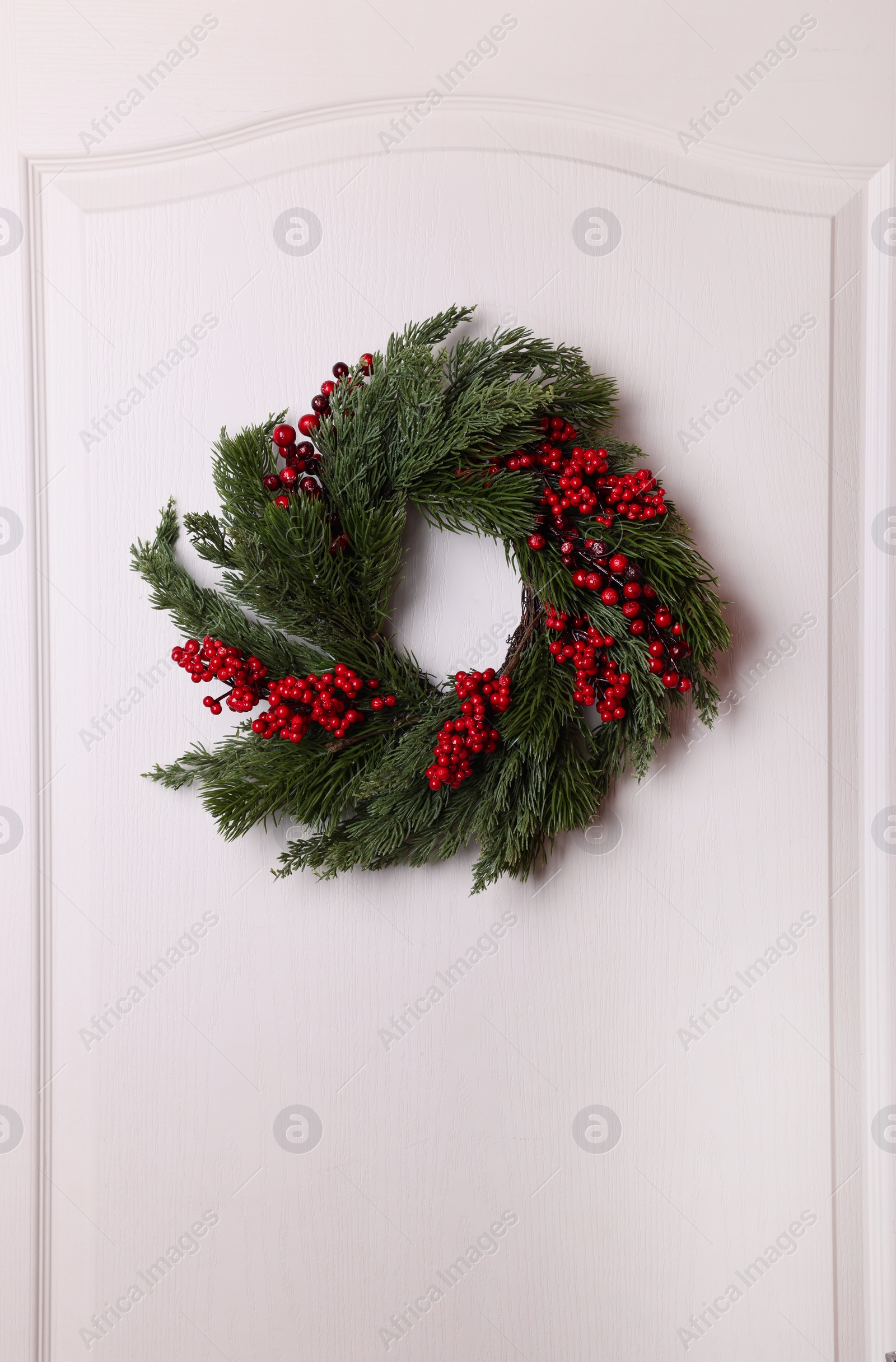 Photo of Beautiful Christmas wreath with red berries hanging on white door