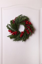 Beautiful Christmas wreath with red berries hanging on white door