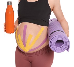 Sporty pregnant woman with kinesio tapes holding water bottle and mat on white background, closeup