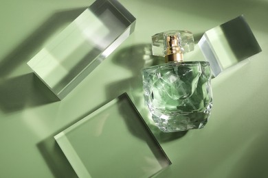 Stylish presentation of luxury perfume in sunlight on olive background, flat lay