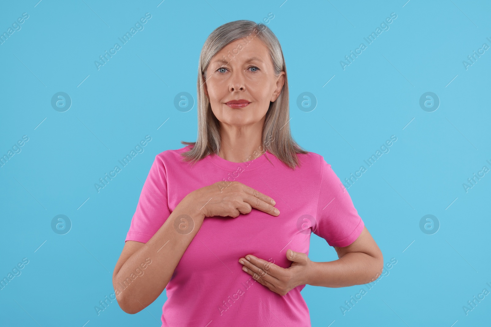 Photo of Beautiful senior woman doing breast self-examination on light blue background