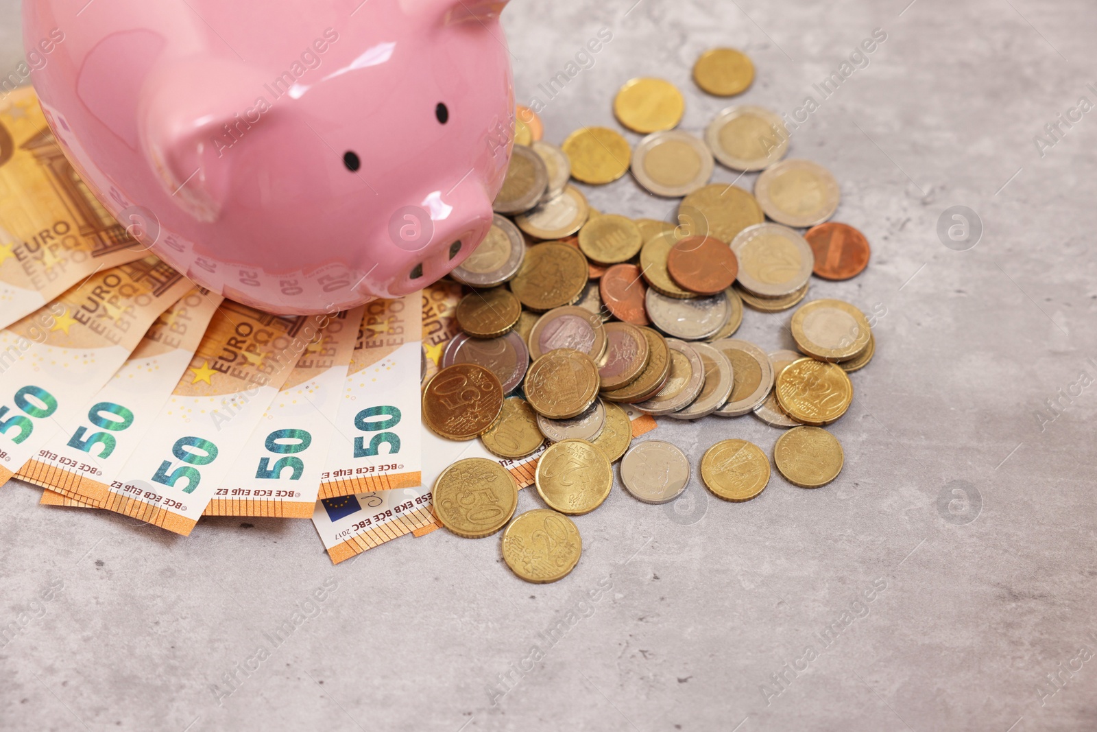 Photo of Piggy bank with euro banknotes and coins on grey table, above view