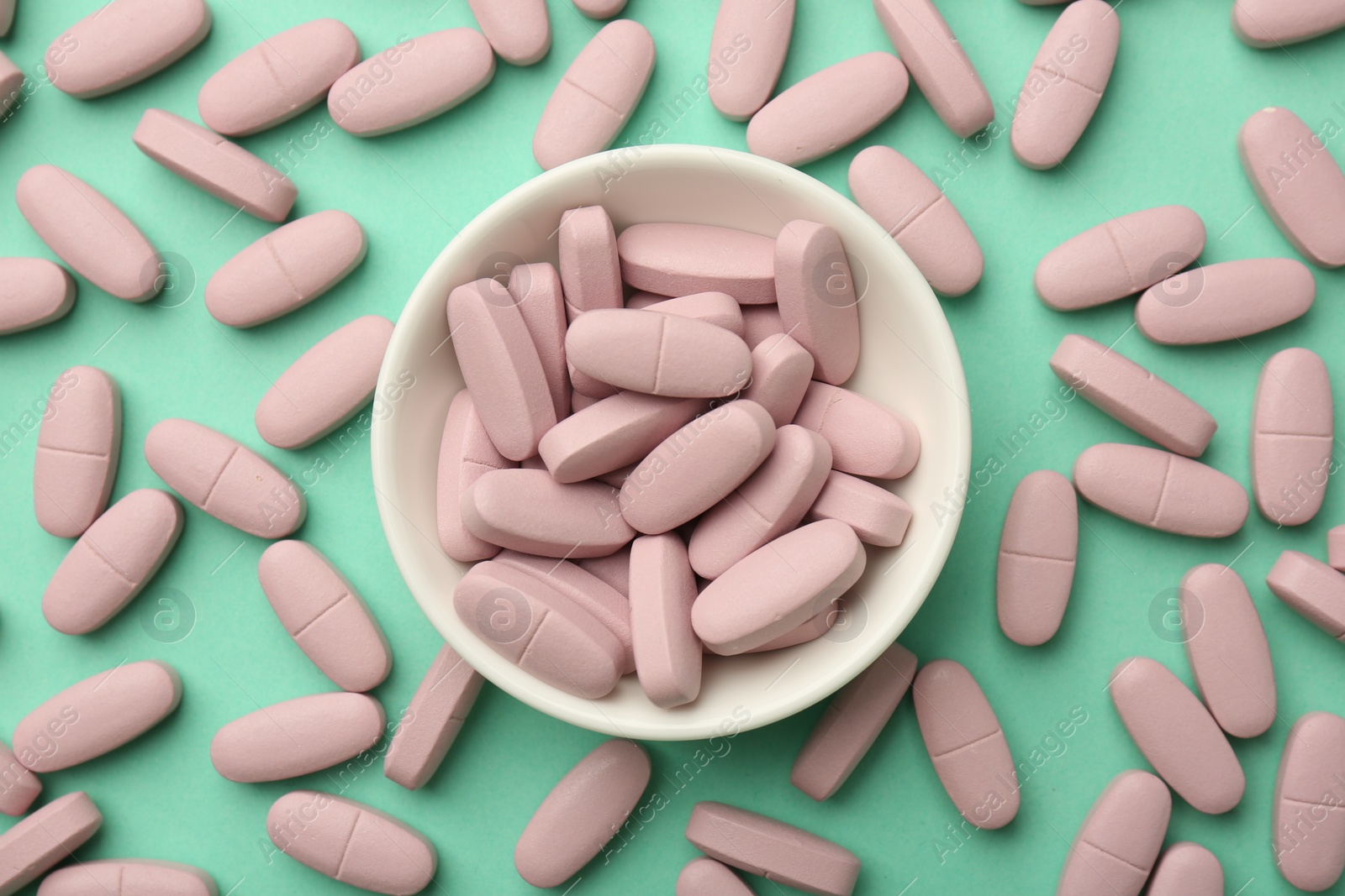 Photo of Pink vitamin capsules and bowl on turquoise background, flat lay