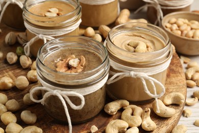 Tasty nut butters in jars and raw nuts on table, closeup