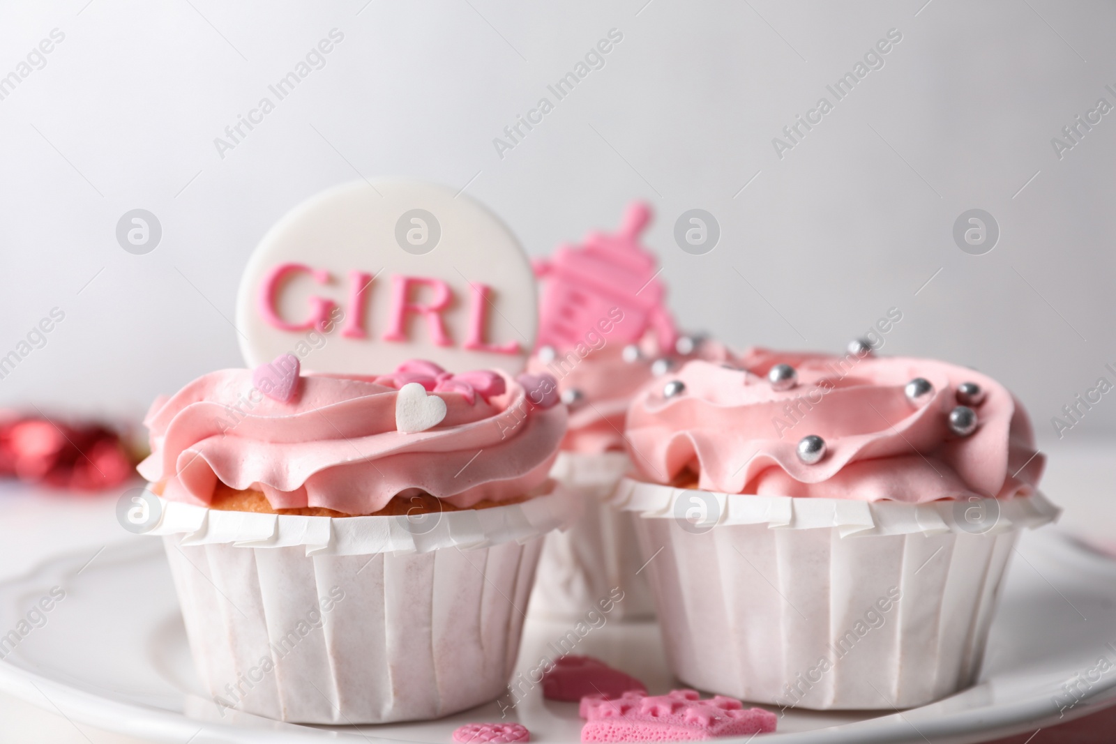 Photo of Delicious cupcakes with pink cream and toppers for baby shower on plate, closeup