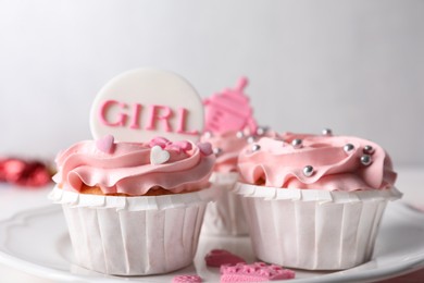 Delicious cupcakes with pink cream and toppers for baby shower on plate, closeup