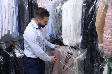 Photo of Dry-cleaning service. Worker taking jacket from rack indoors