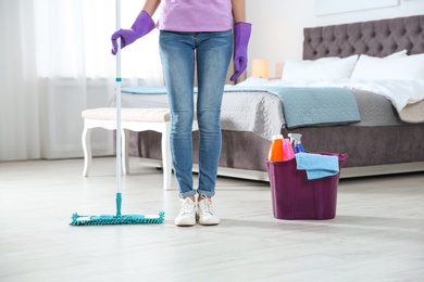 Young woman with mop and detergents in bedroom, closeup. Cleaning service