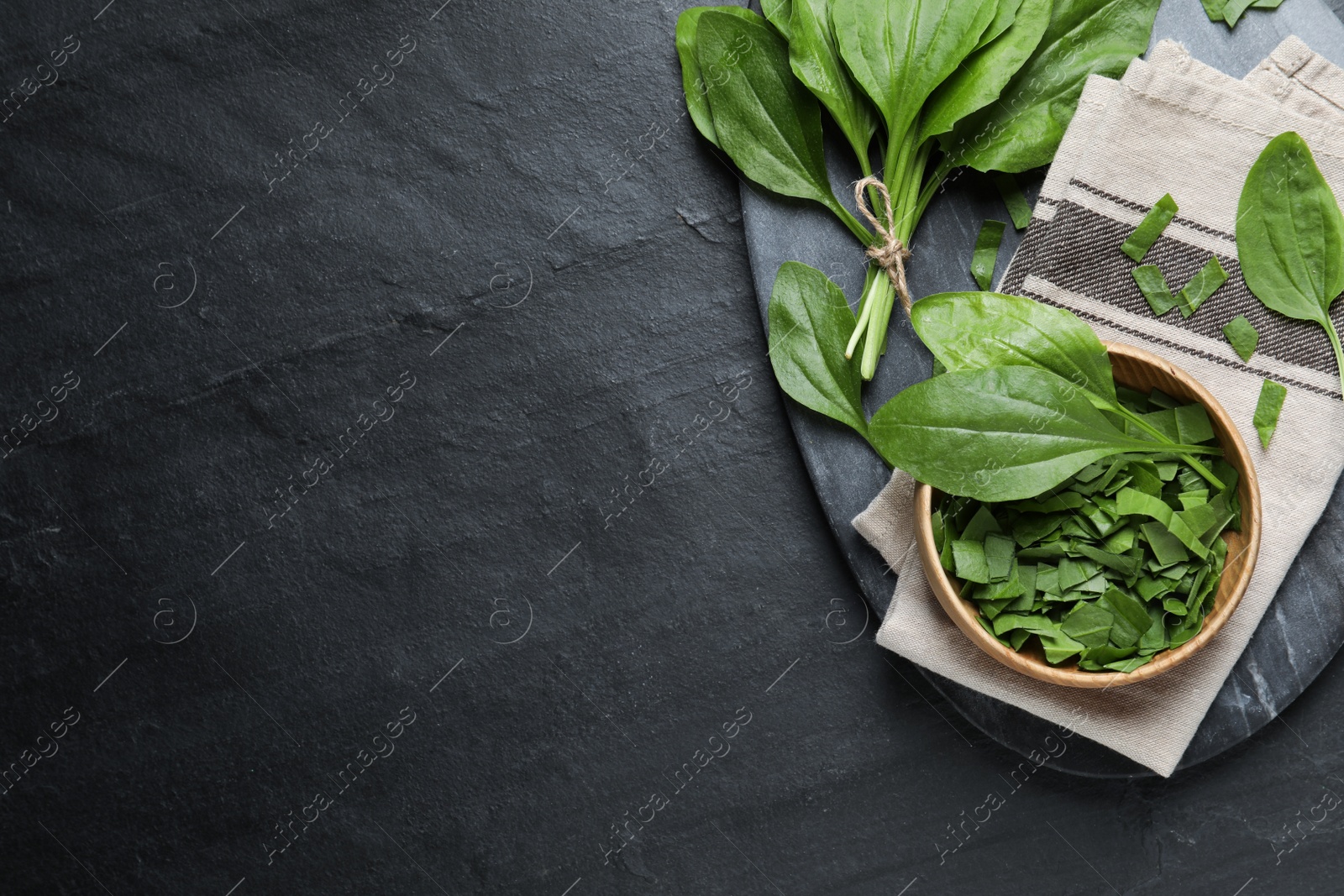 Photo of Broadleaf plantain leaves on black slate table, top view. Space for text