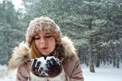 Beautiful woman blowing snow in winter forest. Space for text