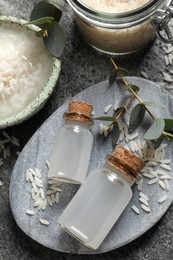 Photo of Glass bottles with rice water and soaked grains on grey table, above view