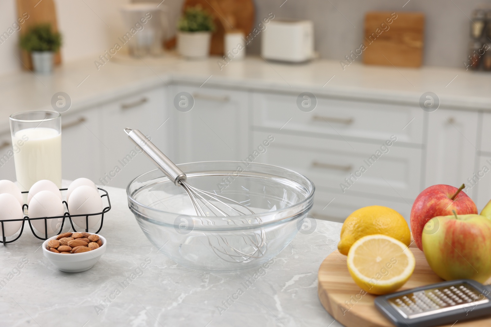 Photo of Metal whisk, bowl, grater and different products on gray marble table in kitchen