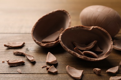 Photo of Broken and whole chocolate egg on wooden table, closeup