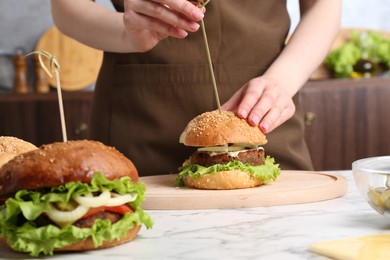 Photo of Woman making delicious vegetarian burger at white marble table, closeup