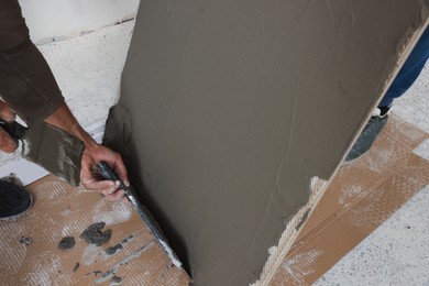 Photo of Workers applying cement on tile indoors, closeup