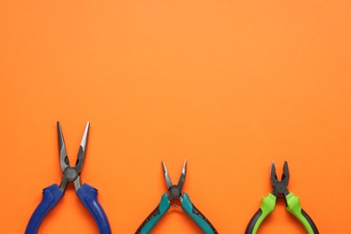 Photo of Different pliers on orange background, flat lay. Space for text