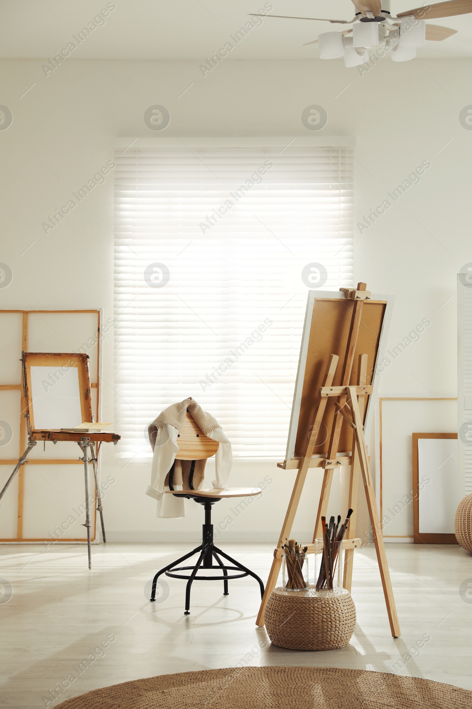 Photo of Modern studio interior with artist's workplace and foldable wooden easel near large window