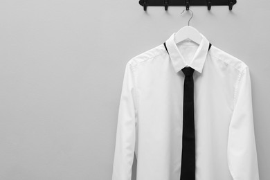 Photo of Hanger with white shirt and black tie on light grey wall, space for text