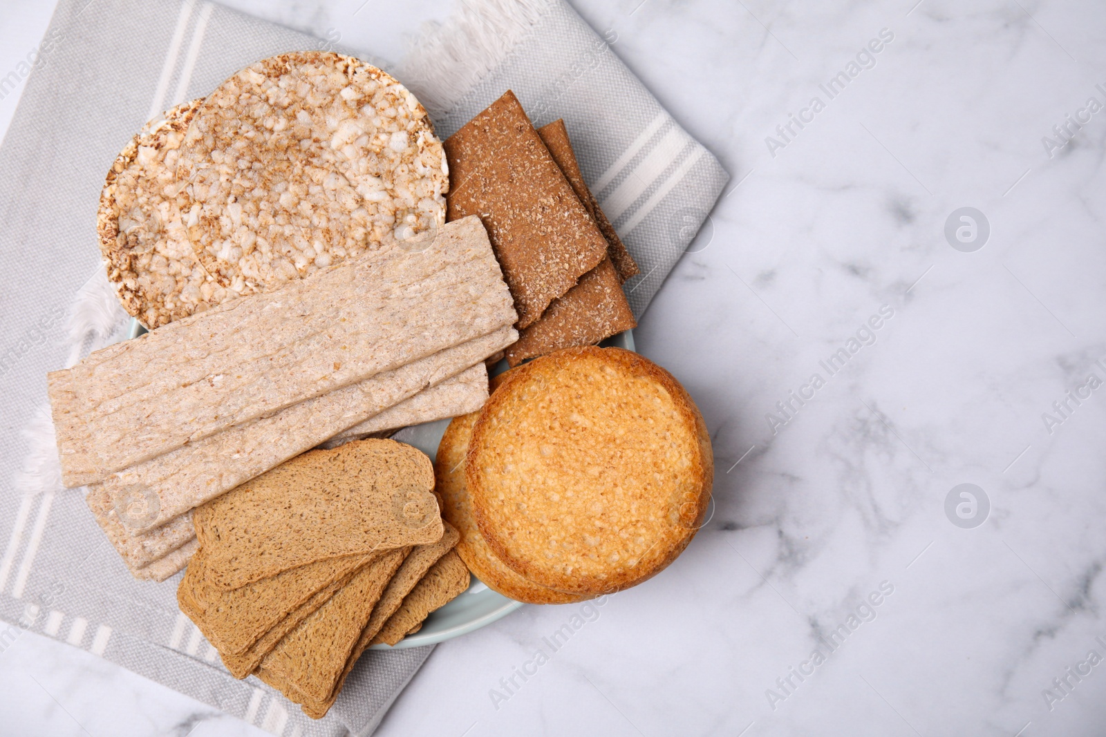 Photo of Rye crispbreads, rice cakes and rusks on white marble table, flat lay. Space for text