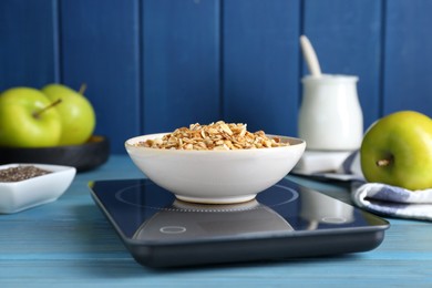 Photo of Electronic scales with granola on light blue wooden table