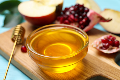 Honey near apple and pomegranate on wooden board, closeup. Rosh Hashanah holiday