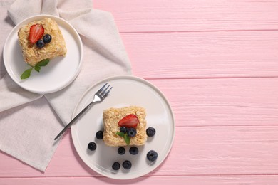 Pieces of delicious Napoleon cake with fresh berries served on pink wooden table, flat lay. Space for text