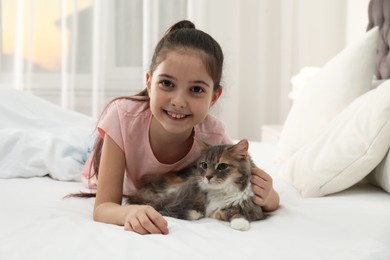 Photo of Cute little girl with cat lying on bed at home. First pet