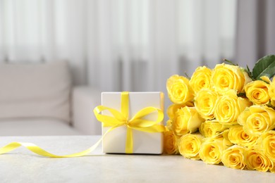 Beautiful bouquet of yellow roses and gift box on light grey table indoors, space for text