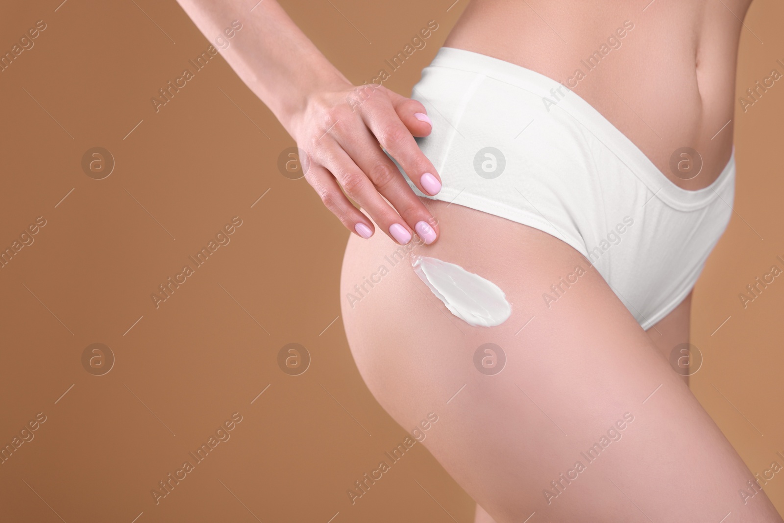 Photo of Woman with smear of body cream on her leg against light brown background, closeup. Space for text