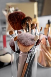 Photo of Set of professional makeup brushes near mirror, closeup