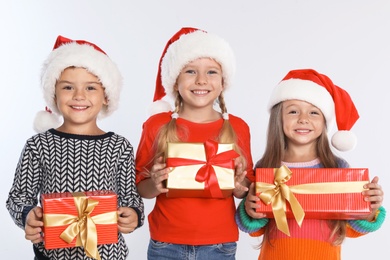 Happy little children in Santa hats with gift boxes on light grey background. Christmas celebration