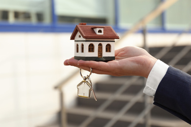 Photo of Real estate agent holding key and house model outdoors, closeup