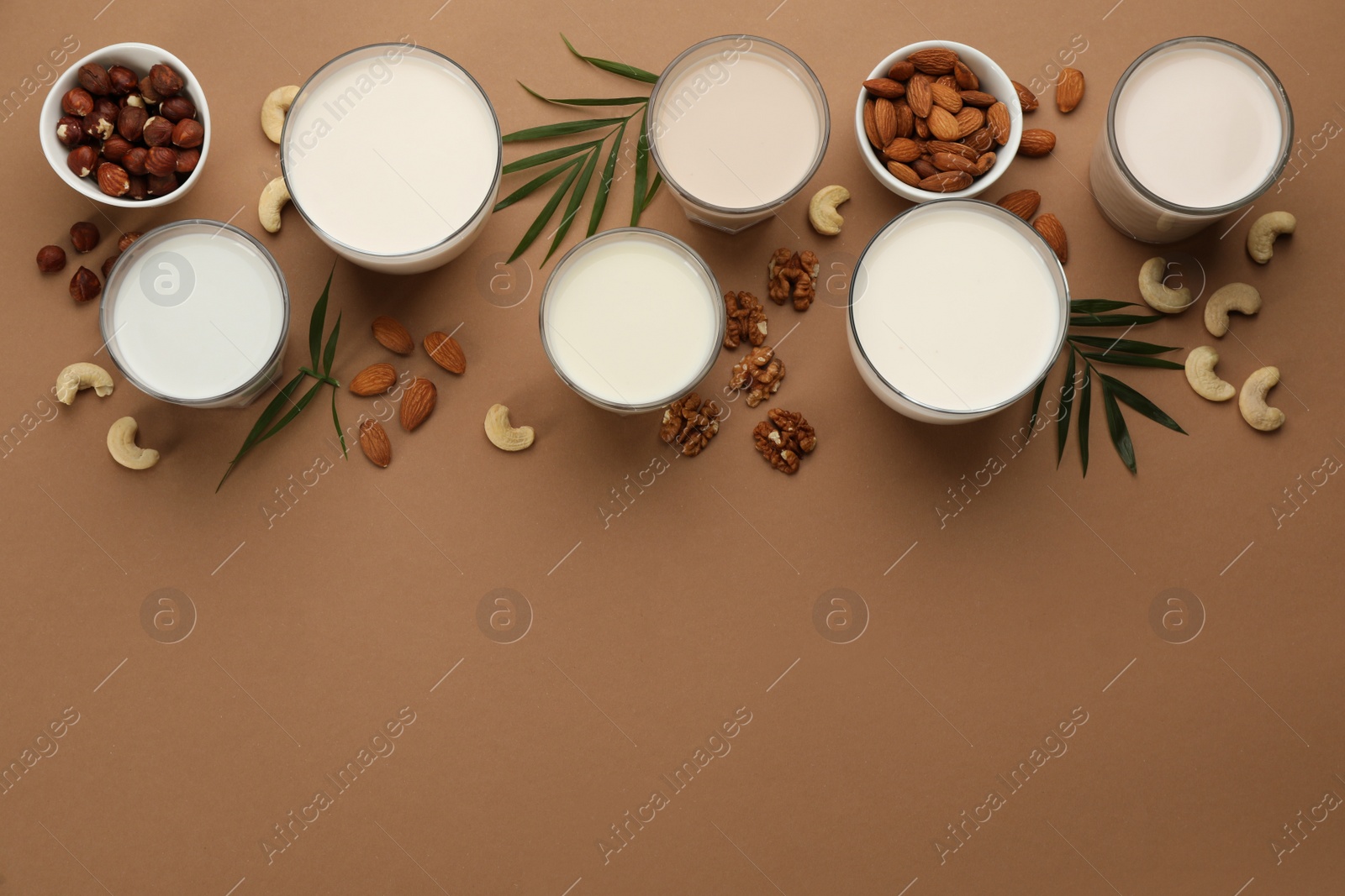 Photo of Different vegan milks and nuts on brown background, flat lay. Space for text