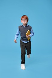 Photo of Smiling schoolboy in glasses with book on light blue background
