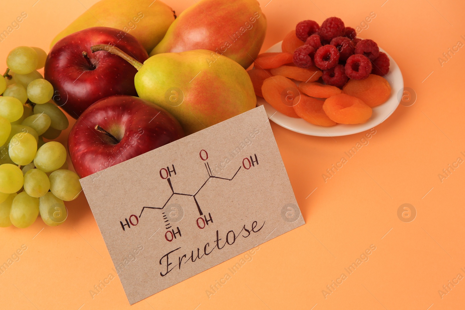 Photo of Card with word Fructose, delicious ripe fruits, raspberries and dried apricots on pale orange background