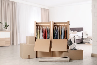 Cardboard wardrobe boxes with clothes on hangers, lamp and carpet in bedroom