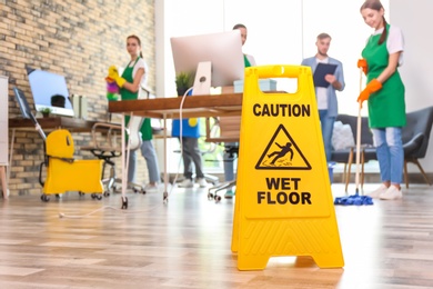 Photo of WET FLOOR sign and team of professional janitors in office