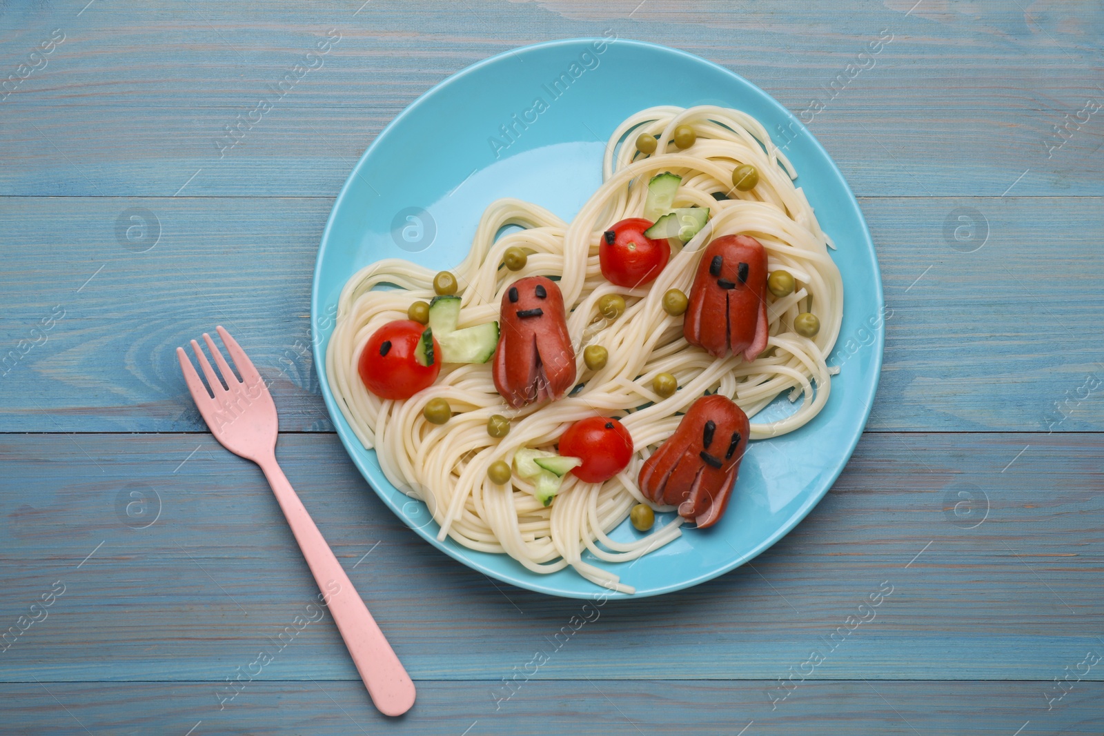 Photo of Creative serving for kids. Plate with cute octopuses made of sausages, pasta and vegetables on light blue wooden table, flat lay