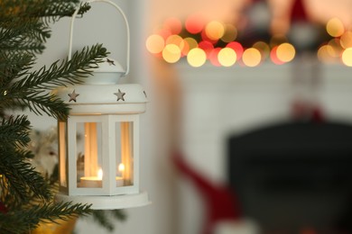 Photo of Christmas lantern with burning candle on fir tree indoors, closeup. Space for text