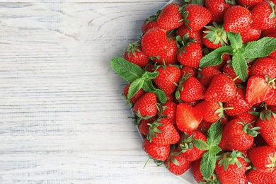 Plate with ripe red strawberries and mint on wooden background, top view