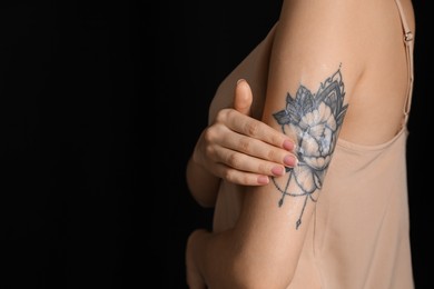 Photo of Woman applying cream onto her arm with tattoo on dark background, closeup. Space for text