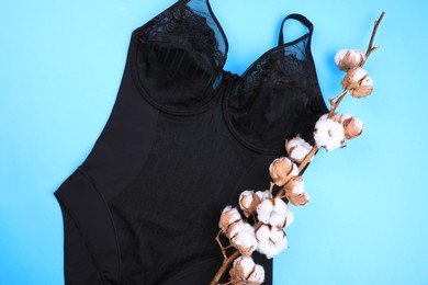 Elegant plus size black women's underwear and cotton flowers on light blue background, flat lay