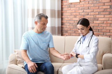 Doctor checking mature man's pulse with fingers at home
