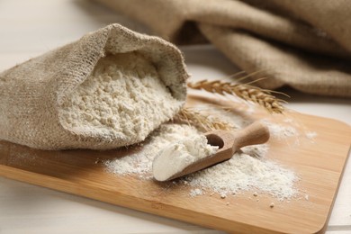 Photo of Sack and scoop of flour with wheat ears on wooden board, closeup